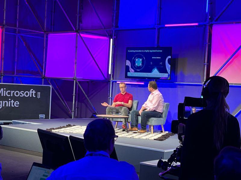 Speakers on a purple-lit stage at Microsoft Ignite, with the audience in the foreground.